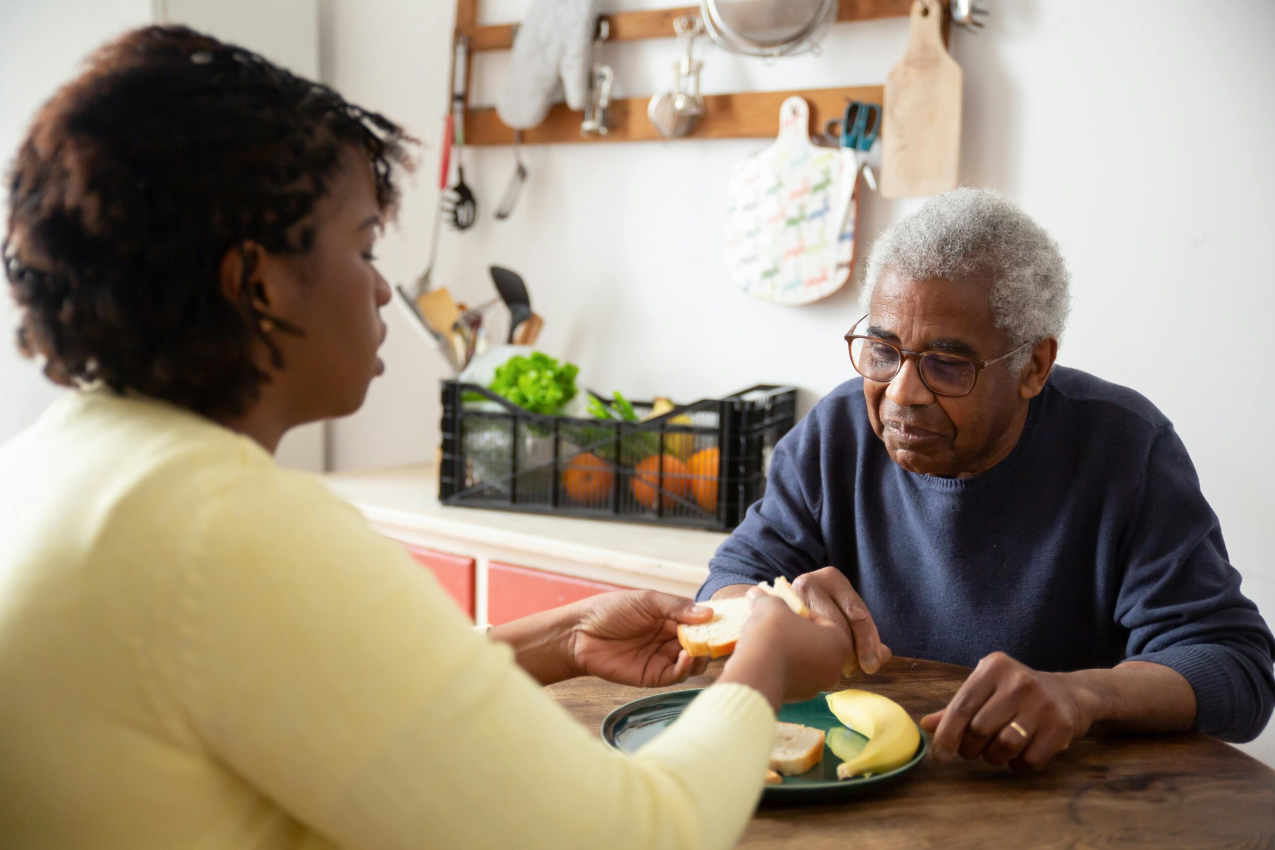 A woman assists an elderly man with meals at home, showcasing care and support.